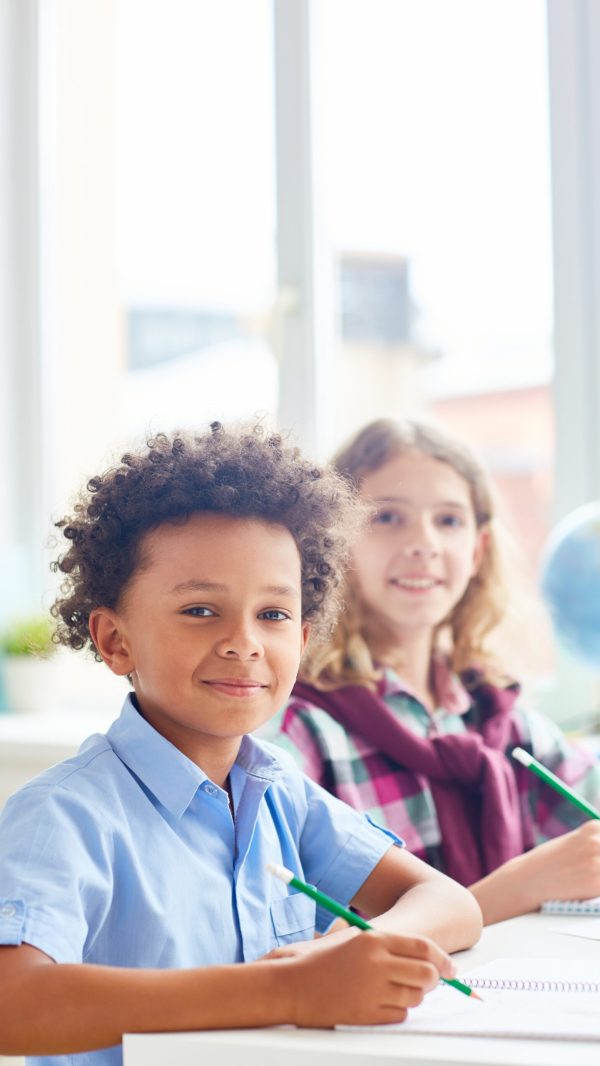 Intercultural boys sitting by desk at lesson of drawing